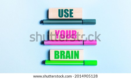 On a light blue background, there are three multi-colored felt-tip pens and wooden blocks with the USE YOUR BRAND