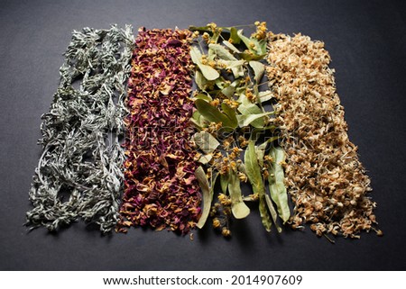 Photography of dried herbs arranged in the line, on the dark background.