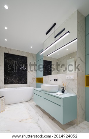 Elegant and spacious bathroom in marble floor and wall tiles with modern blue cabinets and led ceiling lights Royalty-Free Stock Photo #2014924052