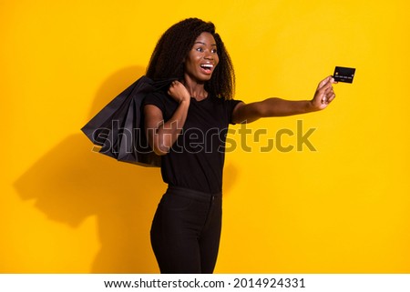 Profile photo of impressed millennial young lady give card wear black outfit hold bags isolated on yellow color background