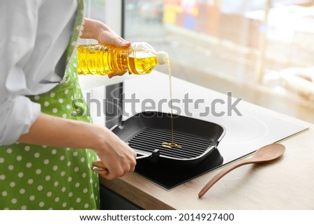 Woman pouring sunflower oil onto frying pan in kitchen Royalty-Free Stock Photo #2014927400