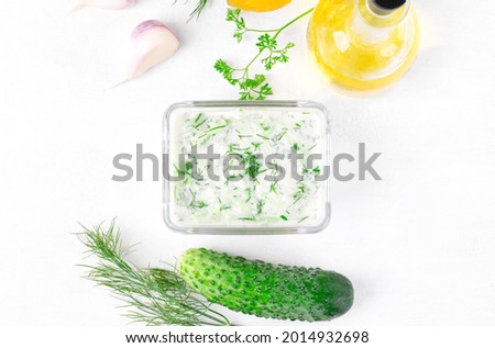 Tzatziki, cucumber sauce with yogurt, garlic, olive oil, herbs and lemon juice on the white table. Greek sauce