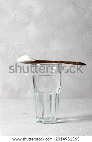 Collagen powder in spoon on glass of water on light gray background. Healthy and antiage concept. Vertical format