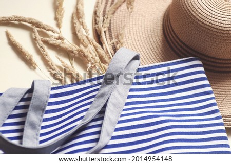 Natural organic cotton striped blue canvas tote bag, straw hat and dry grass. Flat lay summer fashion photo women's accessories