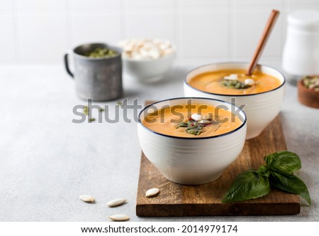 Two bowls of pumpkin cream soup on a wooden board, sprinkled with seeds. Autumn soup. Copy space.