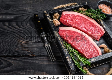 Raw brazilian picanha steak or top sirloin beef meat steak in a wooden tray. Black wooden background. Top view. Copy space