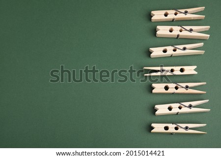 Wooden clothespins on dark green background, flat lay. Space for text
