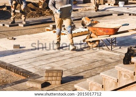 Three construction workers laying interlock driveway pavers and working on a landscaping construction site. Contractors working as team to design and construct large home landscape business project. Royalty-Free Stock Photo #2015017712