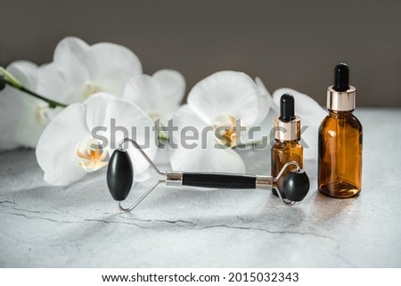 Body and skin care products, dropper bottles and obsidian stone guasha massage roller in the bathroom with orchid flowers, spa cosmetic product branding mockup