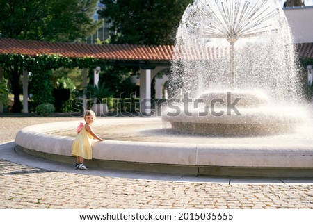Little girl stands near a large spherical fountain in the park