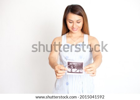 A young beautiful pregnant woman shows a picture of the ultrasound and looks at her tummy with love. Care and tenderness. White background. Screening in pregnancy. White background, space for text