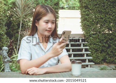 Working outdoor concept a female teenager sitting peacefully in a garden with many green trees while using her device going on the internet.
