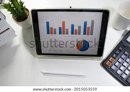 Workplace with tablet pc showing charts and calculator on a wooden work table close-up