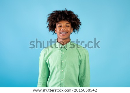 Casual teenage model. Portrait of smiling african american guy in braces looking at camera, wearing mint shirt, posing isolated over blue background, studio shot