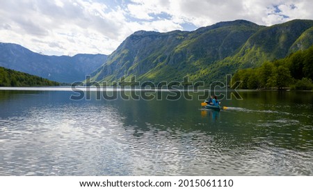 Aerial shot of a two person canoeing on a natural mountain lake, the sun rays breaking through the clouds