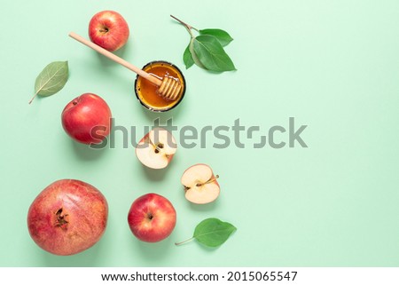 Rosh Hashanah. Apples, pomegranate and honey on a green pastel paper background. Jewish New Year. Traditional Jewish food. Top view, flat lay, copy space