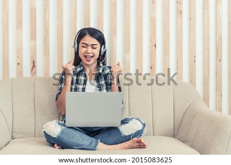 Asian woman in jeans and plaid shirt. Portrait of a young happy female sitting on the couch and working or studying online