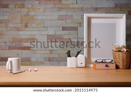 Empty picture frame, coffee cup and pencil holder on wooden table with brick wall.