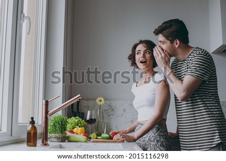 Young amazed fun couple two woman man 20s in casual clothes guy whisper gossip and tells secret behind his hand sharing news cook food in light kitchen at home together Healthy diet lifestyle concept Royalty-Free Stock Photo #2015116298