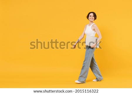 Full length young freelancer happy friendly woman 20s wear white tank top shirt using laptop pc computer chat online browsing surfing internet look aside isolated on yellow color background studio.