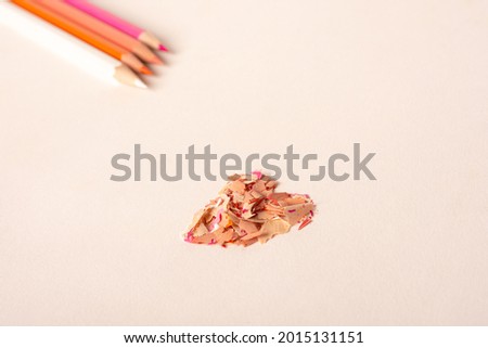 Image of four colored pencil in the left corner and in the center shape of a heart made with the shavings of pencils with a white background.