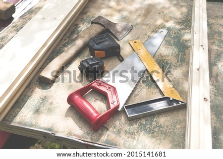 Old vintage hand tools on a wood background, Vintage working tools on a wooden background hand saw, tape measure axe on a table in the garden selective focusing glare from the sun vignetting