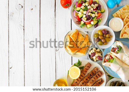 Greek food double border, overhead view on a white wood background. Buffet with gyros wraps, souvlaki, salad, spanakopita and pita with tzatziki.