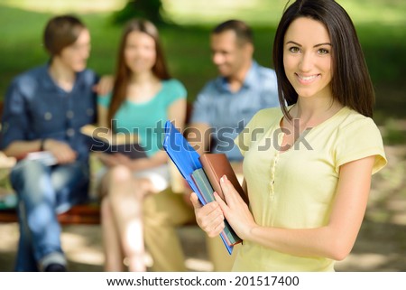 Portrait of a young female student outdoors in park on background of her friends
