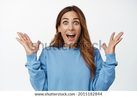 Boom big surprise. Excited happy woman, spread hands sideways and smiling, shouting from joy amazed, react to awesome great news, standing over white background