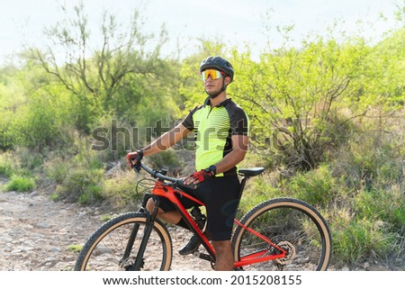 Handsome young man taking a break from pedaling on his mountain bike on a trail and admiring the landscape during the morning