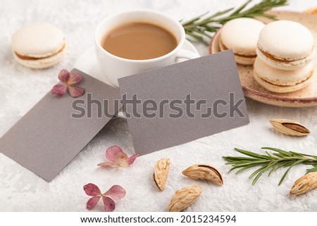 Gray business card mockup with cup of coffee, almonds and macaroons on gray concrete background. Blank, side view, still life.