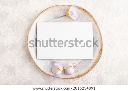 White paper invitation card, mockup with crocus flowers on ceramic plate and gray concrete background. Blank, flat lay, top view, still life, copy space, wedding invitation.