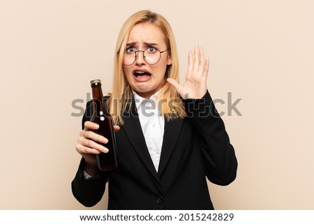 young blonde woman screaming with hands up in the air, feeling furious, frustrated, stressed and upset