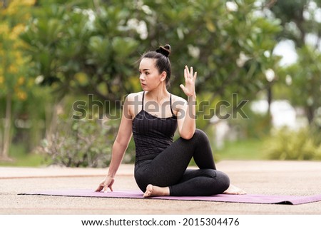 Stock photo of a confident middle-aged Asian woman in sports outfit doing yoga exercise outdoor in the backyard in the morning. Young woman doing yoga exercise outdoor in nature public park