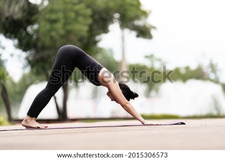 Stock photo of a confident middle-aged Asian woman in sports outfit doing yoga exercise outdoor in the backyard in the morning. Young woman doing yoga exercise outdoor in nature public park