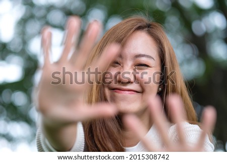 Portrait image of a beautiful young asian woman raising hands and playing with camera in park