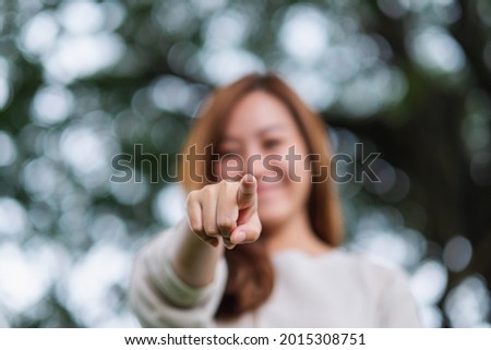 Blurred image of a beautiful young asian woman pointing finger to the camera in the park 
