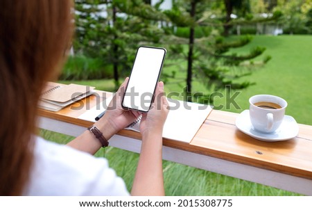Mockup image of a woman holding and using mobile phone with blank white desktop screen in the outdoors