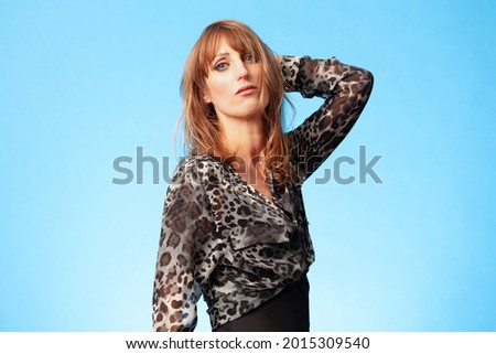 Portrait of an attractive brunette woman wearing a leopard animal print blouse against a blue background