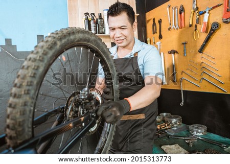 bicycle mechanic in aprons installing wheels while fixing problems on bicycles in workshop