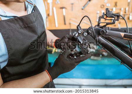 hands of a mechanic wearing gloves installing a rear derailleur while working in a workshop