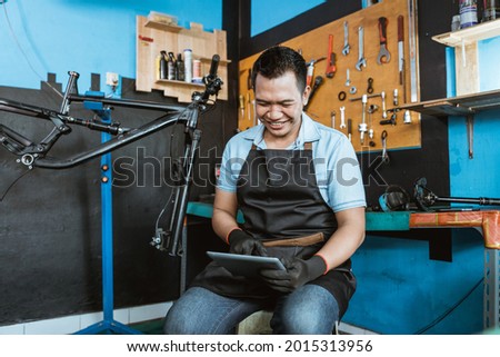 a bicycle mechanic sits using a digital tablet to browse during a break repairing a bicycle in a repair shop