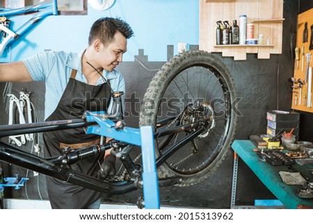 male bicycle mechanic in apron checking the function of freewhells while fixing problems on bicycles in a workshop