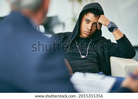 Black male adolescent listening to his counsellor during therapy session at psychotherapist's. Royalty-Free Stock Photo #2015355356