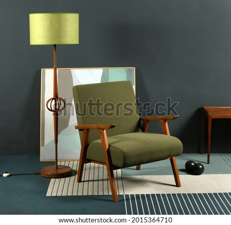 Retro 70s armchair placed on carpet near lamp and abstract picture against gray wall