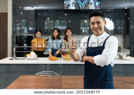 Asian executive master chef in blue apron giving thumb up and enjoy a private group cooking class by standing in front of trainee student chef background. Concepts of culinary course, Kitchen school Royalty-Free Stock Photo #2015368979