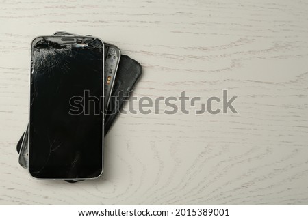 Damaged smartphone on white wooden table, top view with space for text. Device repairing