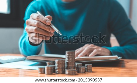 Man counts the coins piled up on the table in preparation to save money, Take note of household financial expenses, Saving money for future growth and knowing how to manage your spending wisely. Royalty-Free Stock Photo #2015390537