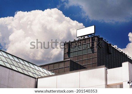 Blank advertising billboard sign on top of a building against blue sky with clouds