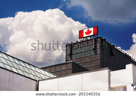 Advertising billboard sign with Canadian flag on top of a building against blue sky with clouds